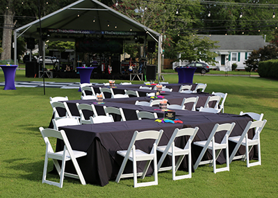 Tables and chairs set up in front of a stage on the Alumni House lawn