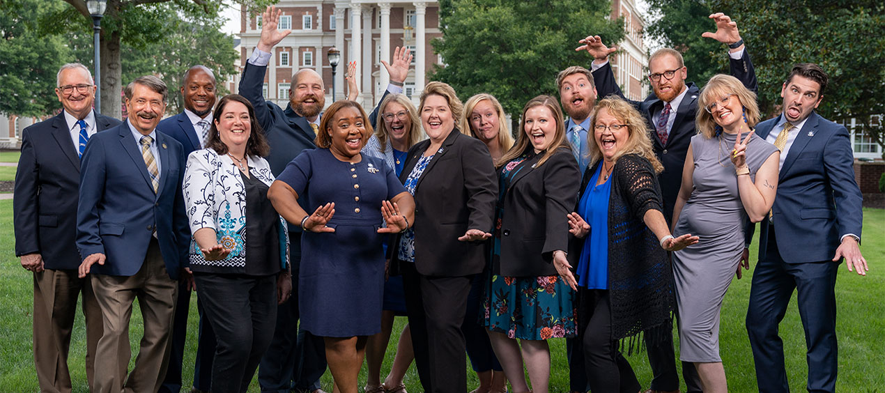 Alumni Society members doing silly poses in front of Christopher Newport Hall